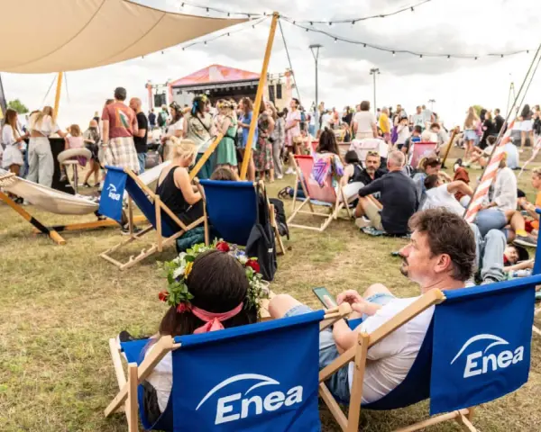 Ludzie odpoczywają na leżakach z logo Enea podczas festiwalu. W tle scena i tłum.