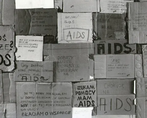 Złe ojciec, zniszczony przez AIDS, błaga o pomoc. Kartony z napisami "AIDS", "SOS", "Ratunku!" i prośbami o wsparcie.