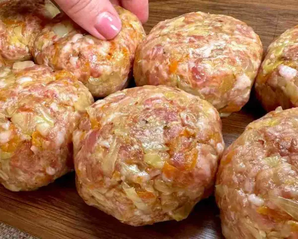 Mani che preparano polpette in bianco, un impasto di carne macinata con verdure, pronte per essere cucinate.