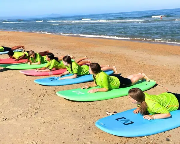 Des adolescents en stage sportif sur la plage, allongés sur des planches de surf, apprenant les bases avant de se jeter à l'eau.