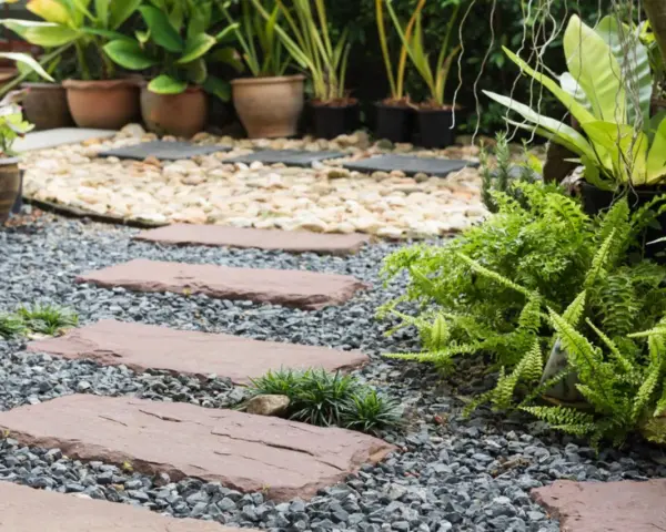 Schrittplatten führen durch einen Kiesgarten. Ein Steingarten anlegen wird hier mit Farnen und Gräsern umgesetzt.