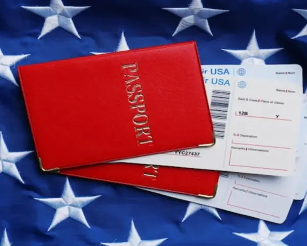 Czerwony paszport i bilety lotnicze na tle flagi USA. Zastanawiasz się, ile kosztuje bilet do USA w dwie strony?