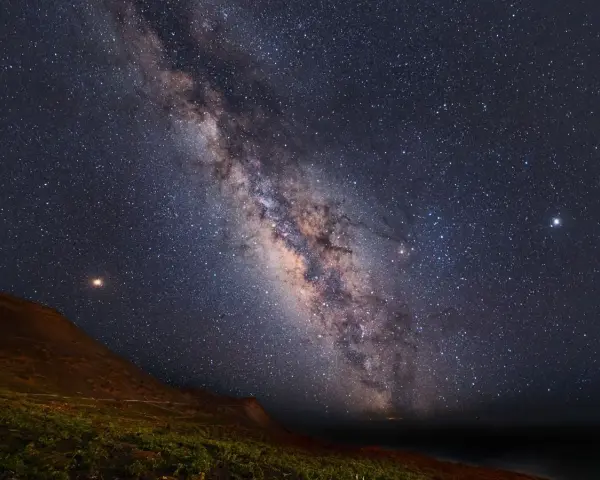Paisaje nocturno en una reserva starlight, con la Vía Láctea cruzando el cielo estrellado sobre una colina y vegetación.