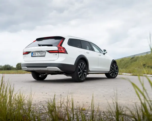 Białe Volvo Cross Country na tle pochmurnego nieba i zielonych wzgórz.