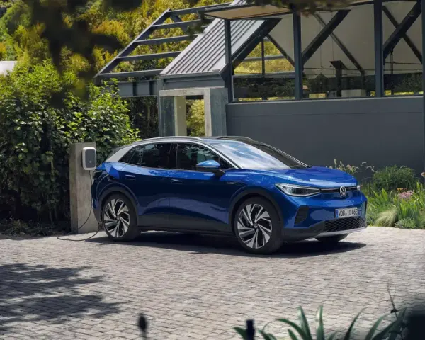Niebieski Volkswagen ID.4 ładuje się przy domu, otoczony zielenią.