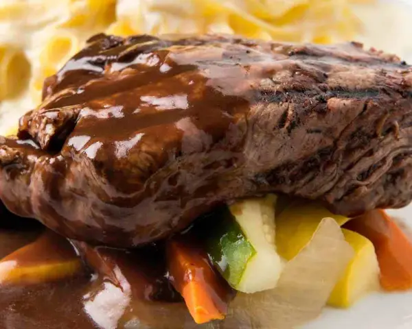 Succulento brasato di manzo nappato con salsa scura, servito su verdure miste e accompagnato da pasta.