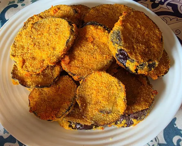 Fette dorate di melanzane in friggitrice ad aria, impanate e croccanti, servite su un piatto bianco.