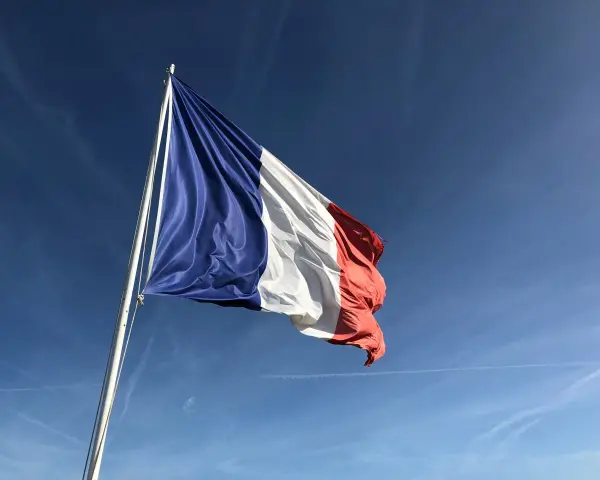 Flaga Francji powiewa na maszcie na tle błękitnego nieba z smugami chmur.