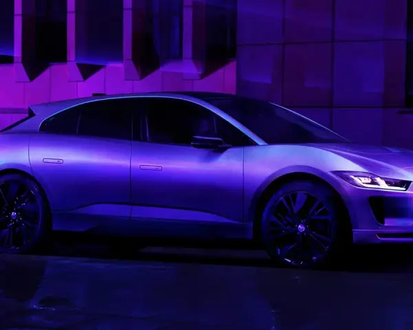Jaguar I-Pace w fioletowym świetle, zaparkowany na mokrej nawierzchni.