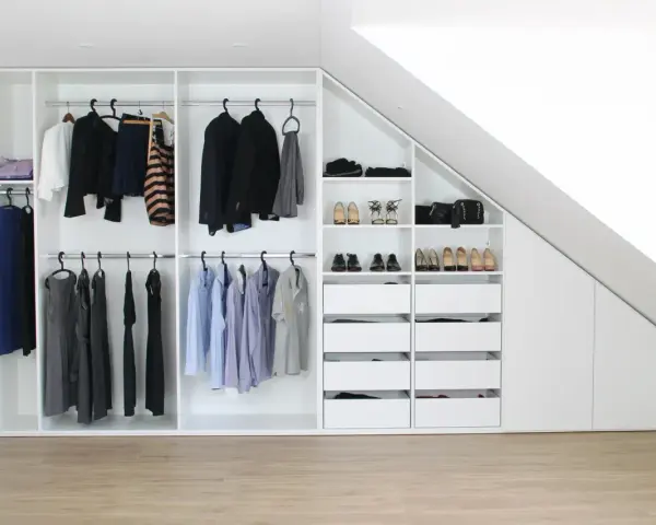 Einbauschrank selber bauen: Weißer Schrank mit Kleiderstangen, Schubladen und Schuhfächern unter einer Dachschräge.