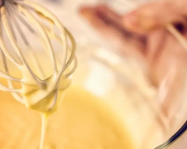 Frusta da cucina che raccoglie una densa pastella per fritti, pronta per creare delizie croccanti.