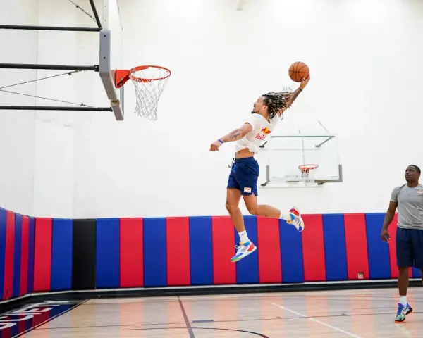 Un joueur de basket-ball en plein saut, ballon en main, effectue un exercice de pliométrie. Un autre joueur observe.