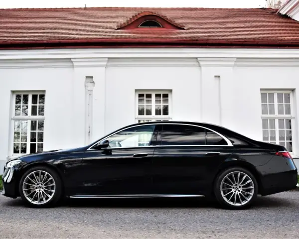 Elegancki, czarny Mercedes S500 lśni na tle białej, zabytkowej fasady z czerwonym dachem.