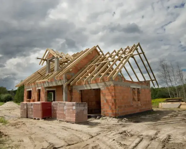 Budowa domu 220m2 w stanie surowym. Ceglane ściany, drewniany dach, materiały budowlane na placu.
