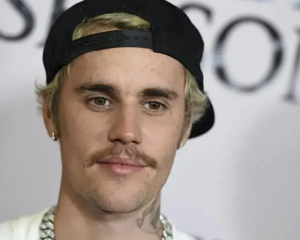 Justin Bieber con un gorra negra y un bigote herradura, luciendo una cadena plateada.