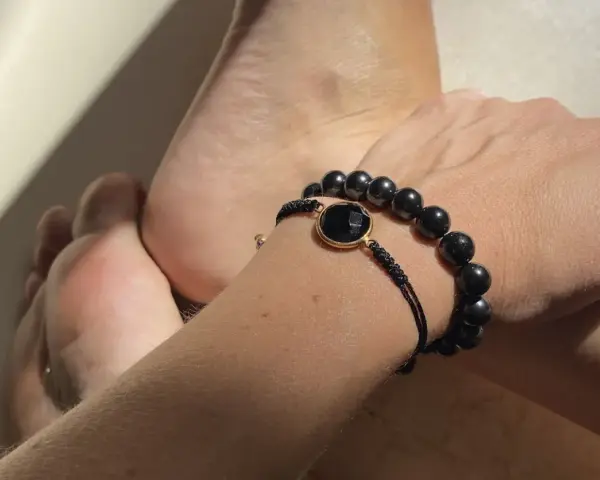 Pulsera con cuentas de obsidiana, una piedra negra protectora, junto a unos pies.