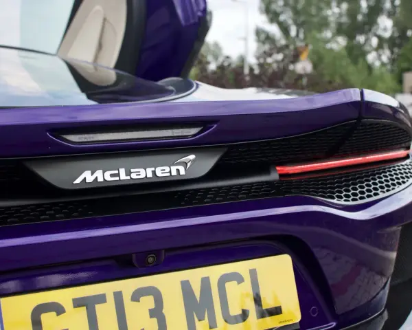 Fioletowy McLaren GT z otwartymi drzwiami, widok na tył z logo i tablicą rejestracyjną.