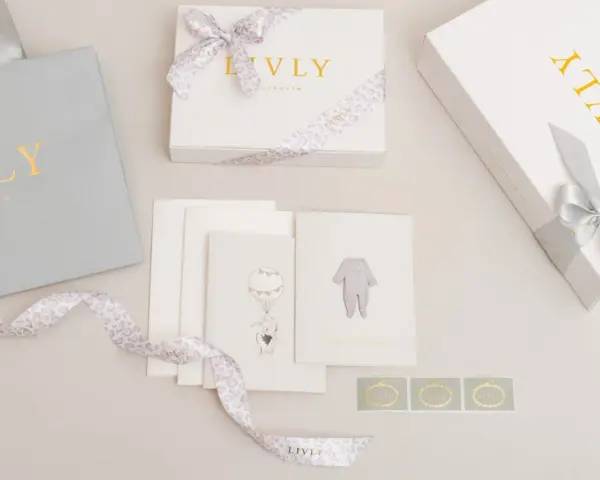 En fin babyshower present tjej med en grå presentpåse, vita presentaskar med guldig text och leopardmönstrat band, samt kort med illustrationer av en elefant i ballong och en babybody.