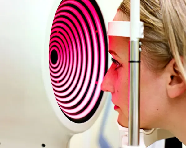 Esame oculistico: una donna guarda un dispositivo che proietta una mappa corneale a spirale rosa e nera.