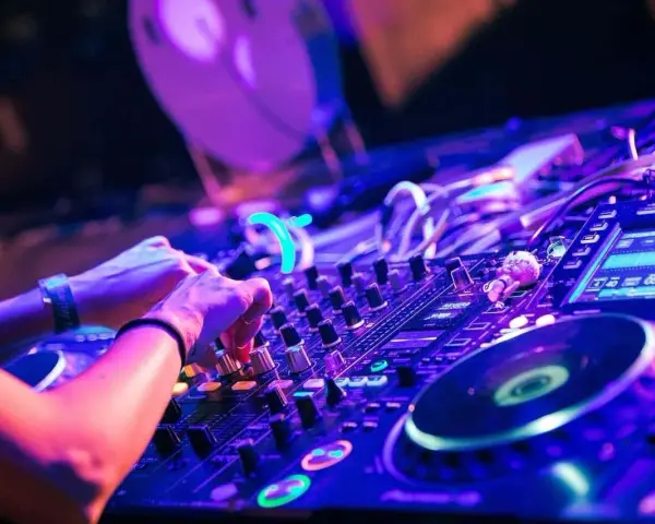 Hände am DJ-Pult, die die Regler für verschiedene techno genres bedienen. Neonlicht und pulsierende Beats.