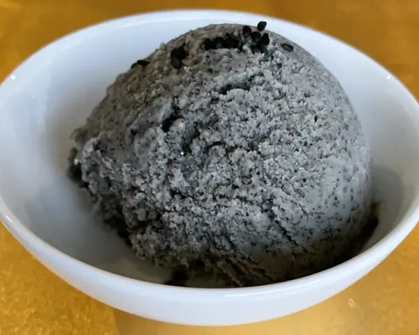 Ein Löffel cremiges Sesam Eis, garniert mit schwarzen Sesamkörnern, in einer weißen Schale.