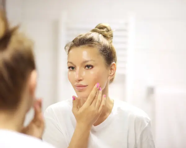 Donna con capelli raccolti applica un siero sul viso. La domanda è: quanti sieri si possono usare insieme per una pelle luminosa?