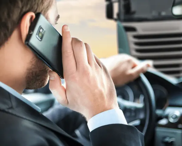 Biznesmen w garniturze rozmawia przez telefon, siedząc za kierownicą ciężarówki. To symbol odpowiedzialności spedytora.