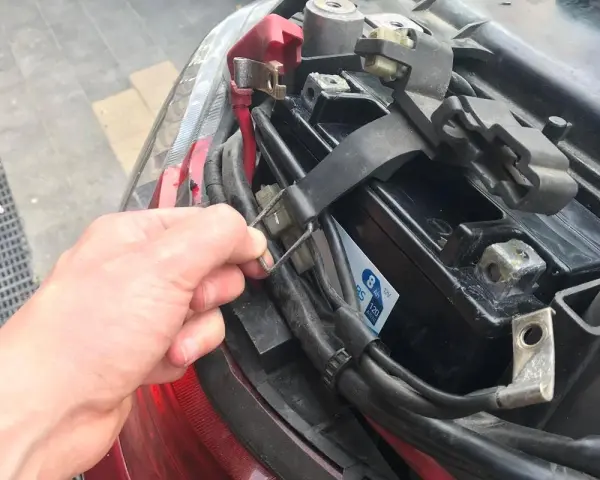 Ręka odkręca mocowanie akumulatora w skuterze. Widać jego umiejscowienie pod siedzeniem.
