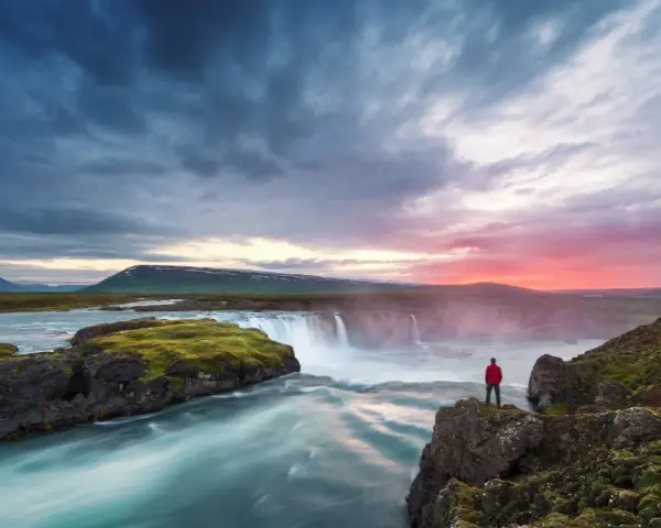 Człowiek w czerwonej kurtce podziwia wodospad na Islandii. Czy Islandia jest bezpieczna? Tak, to piękny i bezpieczny kraj.