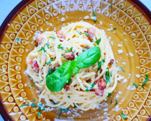 Pyszna carbonara ze szparagami, udekorowana bazylią i posypana parmezanem, na ozdobnym talerzu.