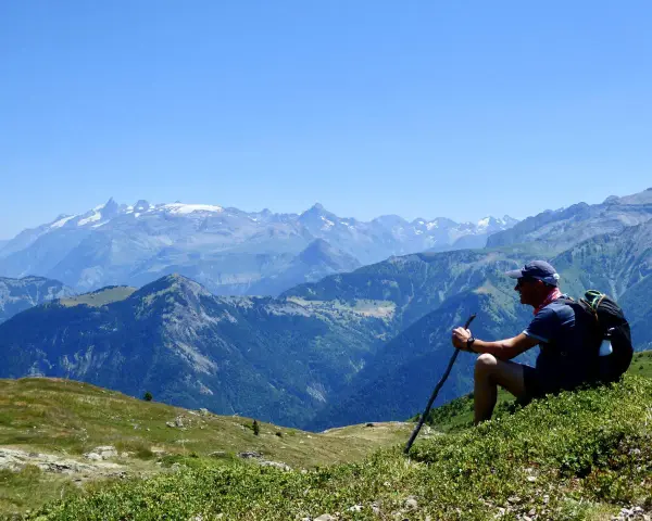 Un randonneur léger profite d'une vue panoramique sur les montagnes. Il est assis sur une colline verdoyante, bâton à la main, admirant le paysage majestueux.
