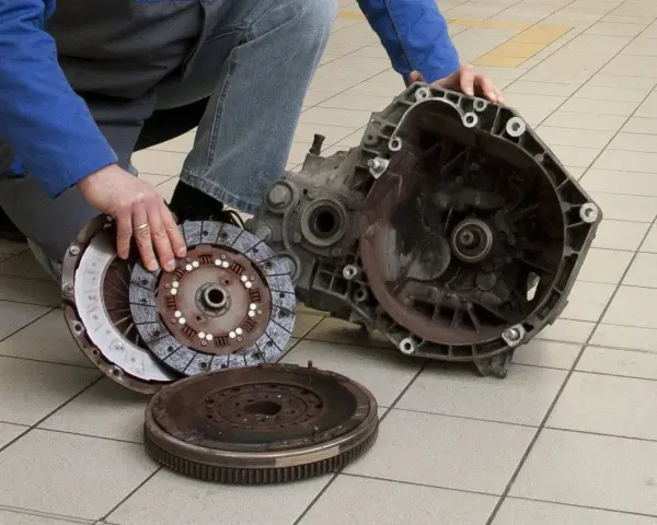 Mechanik prezentuje części po demontażu skrzyni biegów, przygotowując się do wymiany łożyska oporowego.