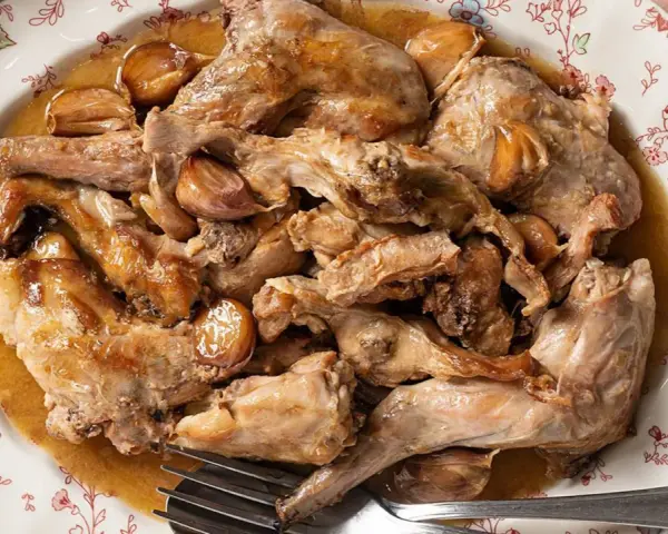 Conejo al ajillo servido en un plato con borde floral, con trozos de carne dorada y dientes de ajo enteros.