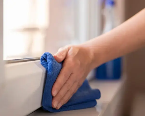 Mano pulisce davanzale in PVC effetto legno con panno blu. Scopri come pulire pvc effetto legno per mantenerlo come nuovo.