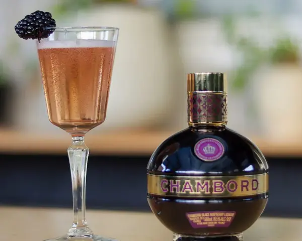 Chambord likier jak pić? Elegancki kieliszek z różowym drinkiem i jeżyną obok butelki likieru. Idealny na specjalne okazje.