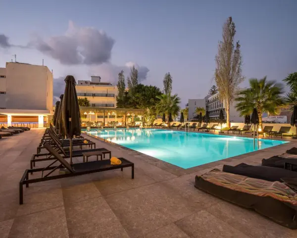Basen hotelowy oświetlony nocą, leżaki i palmy. Idealne miejsce na relaks, zgodnie z licznymi heronissos hotel opinie.