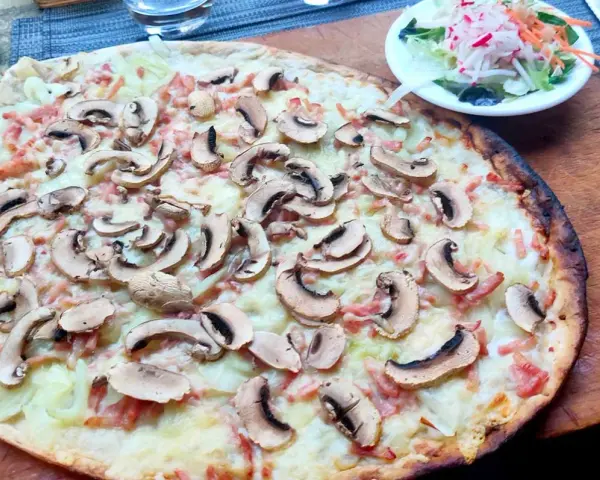 Tarta flambeada con champiñones y bacon, servida sobre tabla de madera. Una pequeña ensalada acompaña.
