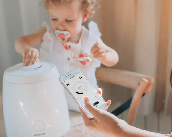 Niña interactúa con humidificador mientras una mano controla la app para humidificar el ambiente.