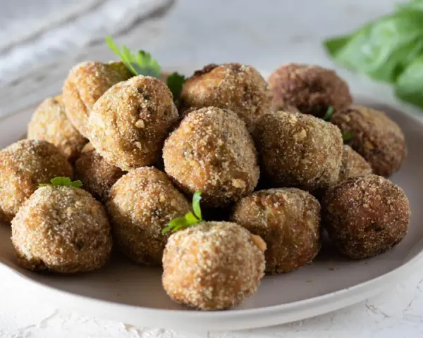 Un piatto pieno di polpette di melanzane dorate e croccanti, guarnite con prezzemolo fresco.