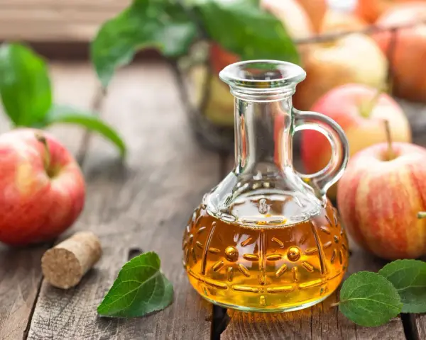 Aceto di mele in un decanter, mele rosse e foglie verdi su un tavolo di legno. Un rimedio naturale per sapere come eliminare i funghi della pelle velocemente.