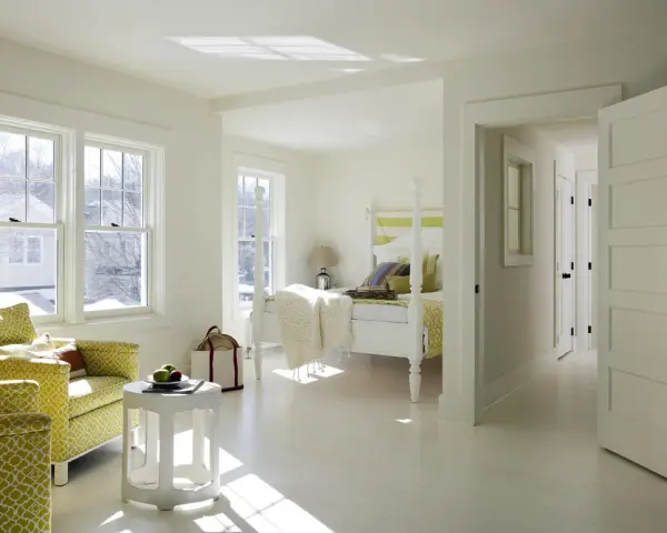 Luminosa camera da letto con **colore pareti bianco caldo**, due poltrone gialle, letto a baldacchino e luce solare che filtra dalle finestre.