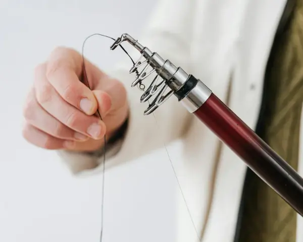 Dłoń trzyma żyłkę przy szczytówce wędki spinningowej.