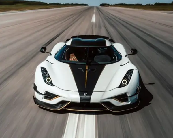 Biały Koenigsegg Regera z czarnym pasem i złotymi akcentami pędzi po pasie startowym, zostawiając za sobą smugę prędkości.