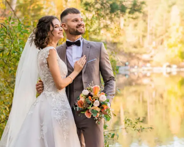 Para młoda w jesiennym lesie, z bukietem w dłoni pana młodego. Ich ślub bez zmiany nazwiska to początek wspólnej drogi.