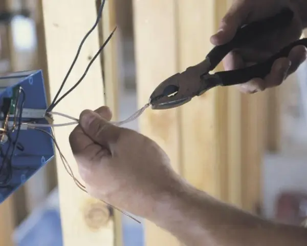 Ręce przycinają przewody do skrzynki elektrycznej. To kluczowy krok, by dowiedzieć się, jak zostać elektrykiem.