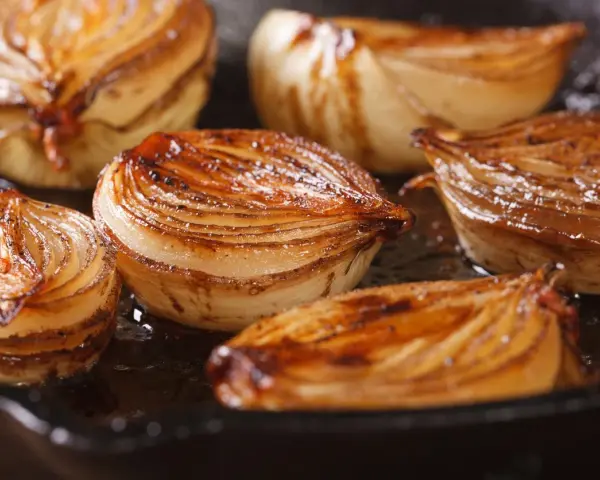 Moitiés d'oignons caramélisés, dorés et juteux, cuisant dans une poêle.