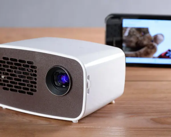 Kleiner Beamer mit Handy verbinden für Heimkino. Ein Smartphone zeigt ein Bild, während der Beamer bereit ist.