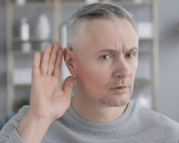 Mężczyzna z siwymi włosami przykłada dłoń do ucha, próbując usłyszeć. Czy to początek zawalu ucha?