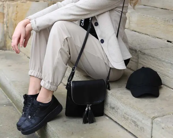 Stylisches flugzeug outfit damen: beige Hose, Blazer, schwarze Sneaker, Tasche und Cap. Perfekt für die Reise.