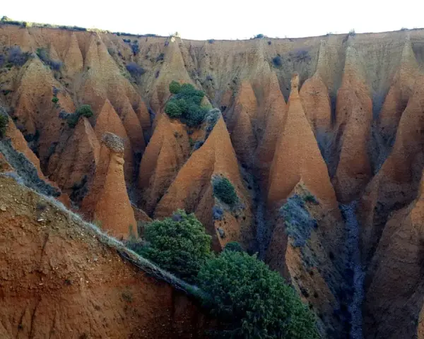 Paisaje erosionado con formaciones cónicas de tierra rojiza, vegetación escasa y un camino que parece el pontón de la oliva ruta circular.